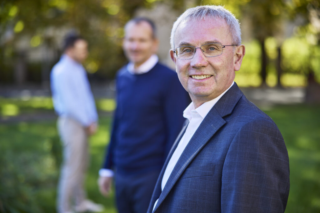 CEO i AFSN Flemming Sindberg står i front hvor man skimter COO og en annen ansatt i bakgrunnen. De står i et parkområdet med gress og trær i bakgrunnen.